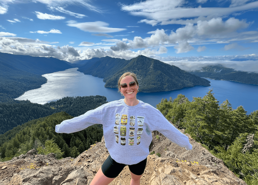 Mount Storm King in Port Angeles, Washington on a sunny day with a hiker at the top celebrating the good weather and making it!
